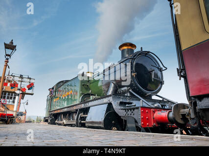 Niedrige Winkel Nahaufnahme der vintage UK Dampflok am Morgen Frühling Sonnenschein Puffing Dampf warten auf vintage Station, Zugfahrer Blick aus dem Taxi. Stockfoto