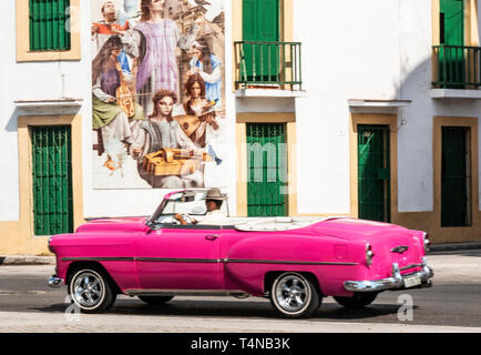 Havanna, Kuba - vom 25. Juli 2018: Eine alte Rosa Cabrio fahren die Straße hinunter, vorbei an einem Wandbild an einem Gebäude in Havanna, Kuba. Stockfoto