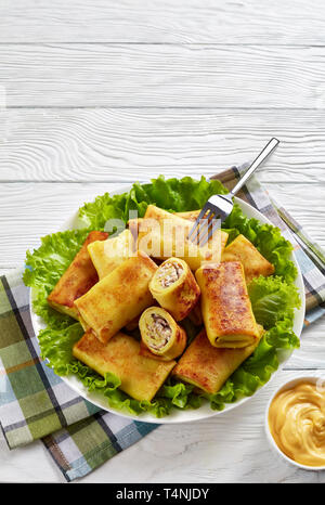 Crepe Brötchen mit gemahlenem Hühnerfleisch und Pilzen füllen serviert auf einem schlechten frische Salatblätter auf einem weißen Teller auf einem Holztisch mit Käse sauc Stockfoto