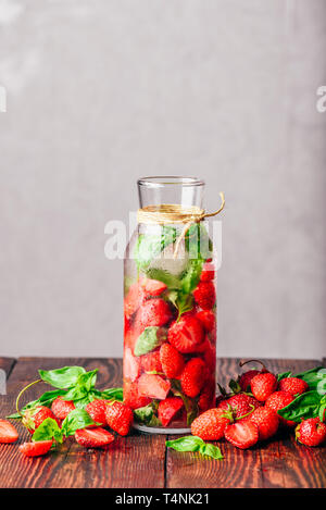 Flasche Wasser hineingegossen mit frischen Erdbeeren und Basilikum. Zerstreut Zutaten auf Holztisch. Vertikale Ausrichtung und Kopieren. Stockfoto
