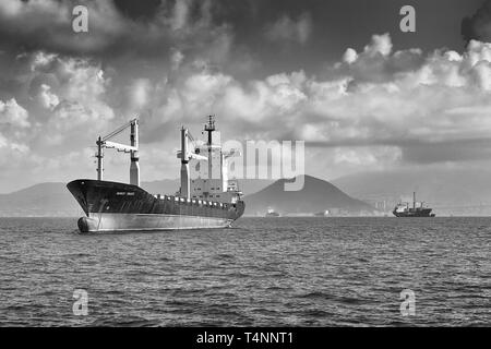 Moody Schwarz-weiß-Foto des Fracht-/Containerschiffs, MÜNCHNER HÄNDLER, in-Ballast und westlich von Victoria Harbour, Hongkong. Stockfoto