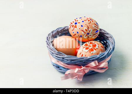 Ostern Hintergrund mit bemalten Eier in den kleinen blauen Weidenkorb mit rosafarbenen Seidenband. Frohe Ostern Grußkarte, kopieren. Stockfoto