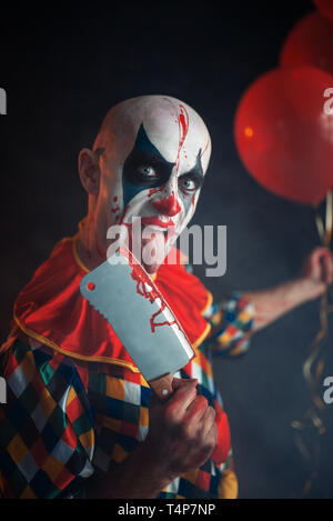 Beängstigend blutigen Clown leckt die Messerklinge. Mann mit Make-up im Halloween Kostüm, verrückte Maniac hält der menschlichen Hand Stockfoto