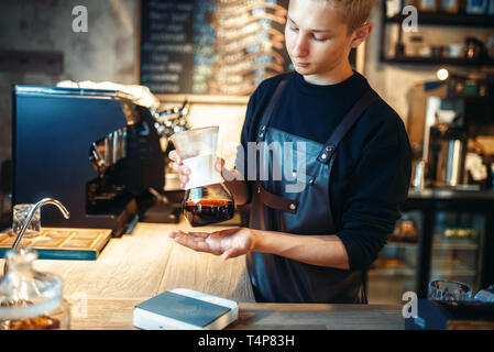 Junge männliche Barista macht frischen Espresso im Cafe. Barkeeper arbeiten in der Cafeteria, Barmixer bereitet schwarzen Kaffee Stockfoto