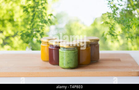 Babynahrung, gesundes Essen und Ernährung Konzept - Gemüse oder Obst pürieren, die in Gläsern auf hölzernen Tisch über grüne natürlichen Hintergrund Stockfoto