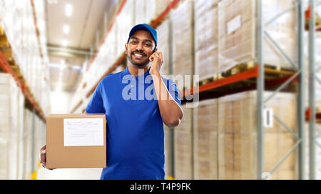E-mail Service, Kommunikation und Versand Konzept - glückliche indischen Delivery Man oder Lagerarbeiter mit Smartphone und Paketbox in blauer Uniform über g Stockfoto