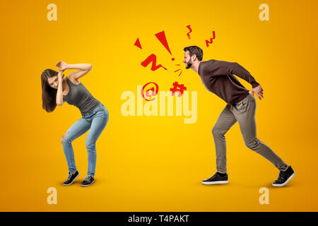 Junge brünette Mädchen mit lässigen Jeans und T-Shirt selbst Schutz von wütenden Schreien Mann auf gelbem Hintergrund Stockfoto