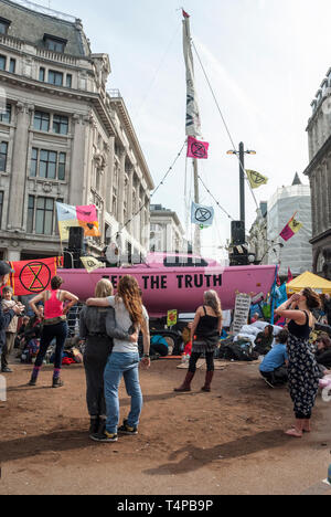 "Demonstranten Aussterben Rebellion "Embrace und Tanz wie Oxford Circus besetzen; hinter ist ein helles Rosa Yacht mit einer "Wahrheit" zu unterzeichnen. Stockfoto