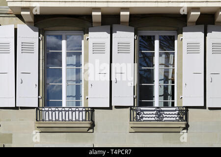 Details der alten mittelalterlichen Gebäude. Das Gebäude hat beige Betonwände und die Fensterrahmen sind weiß und aus Holz. In Nyon fotografiert. Stockfoto