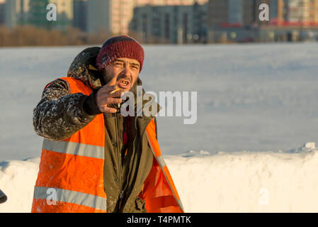 Porträt eines Arbeitnehmers in einer grünen Jacke mit Kapuze auf dem Kopf in einem orange Warnweste und einer Zigarette in der Hand Stockfoto