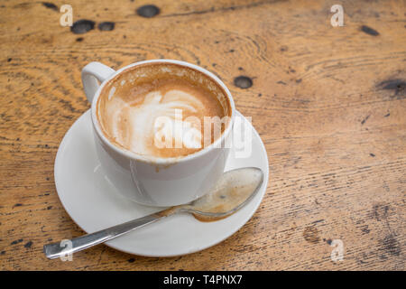 Eine Tasse Latte in eine Schale mit einem Löffel auf einer rustikalen Holztisch Stockfoto