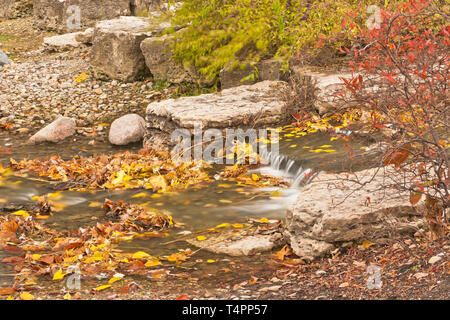 Rote, braune und gelbe Blätter hinzufügen Sprenkelung der Farbe zu den Felsen und Wasserfällen der Pfosten - Abfertigung See Stromschnellen in St. Louis Forest Park auf einem Stockfoto