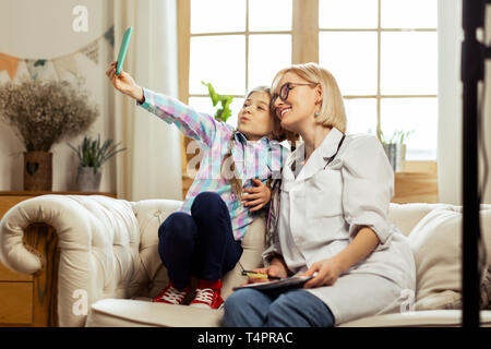 Ein selfie mit einem Arzt. Verführerisch leuchtenden strahlend schönen blonden Kinderarzt selfies, mit einem kleinen süßen Wiederherstellung kranken fröhliches Mädchen. Stockfoto