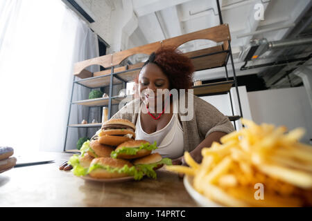 So lecker. Fröhliche brunette Ausdruck Positivität und Hamburger starrte Stockfoto
