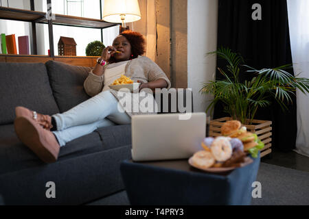 Home Rest. Fröhliche Frau hält Teller mit Essen, während Sie Film Stockfoto