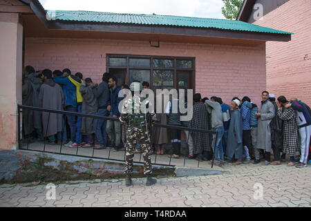 Srinagar, Kashmir. 18 Apr, 2019. Eine Indische paramilitärischen Trooper wacht als Kaschmir Wähler in einer Warteschlange stehen, ihre Stimmen in der zweiten Phase der allgemeinen Wahlen in Indien zu werfen, vor einem Wahllokal in der Nähe von Srinagar Stadt, der Sommer Hauptstadt von Kaschmir, 18. April 2019. Credit: Javed Dar/Xinhua/Alamy leben Nachrichten Stockfoto