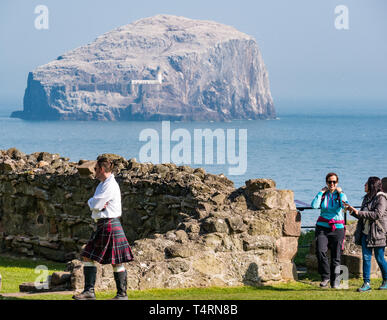 Tantallon Castle, North Berwick, East Lothian, Schottland, Vereinigtes Königreich, 19th. April 2019. Großbritannien Wetter: Historische Umgebung Schottlands zerstörte Burg aus dem 14th. Jahrhundert. Die Vorhangmauer Burg mit Blick auf die größte Nördliche Gannetkolonie auf dem Bass Rock im Firth of Forth. Die Tölpel vereinen sich wieder und bauen Nester. Ein Reiseführer mit einem Kilt zeigt zwei weibliche Touristen rund um das Schloss Stockfoto