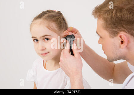 Die junge sympathische otolaryngologist untersucht die Ohren der ein Mädchen - ein Mädchen im schulpflichtigen Alter, Stockfoto