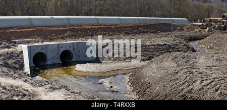 Große konkrete Kanalrohre und Haufen von Sand mit Spuren von schwerer Ausrüstung Räder auf einem Abwasserkanal Baustelle in den Wald. Stockfoto