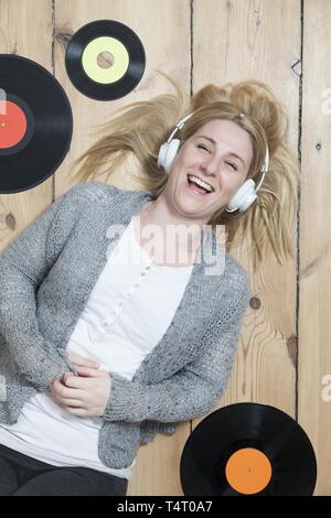 Junge blonde Frau liegend auf dem Holzboden, umgeben von Aufzeichnungen Stockfoto