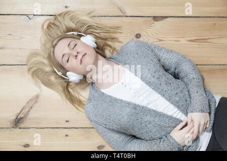 Junge blonde Frau liegend auf dem Holzboden, umgeben von Aufzeichnungen Stockfoto