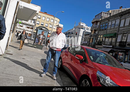 Ein schneidiger älteren Mann im weißen Jacke und Jeans trägt einen weißen Hut stehend Beobachten durch ein rotes Auto Praça do Exército Libertador Porto KATHY DEWITT Stockfoto