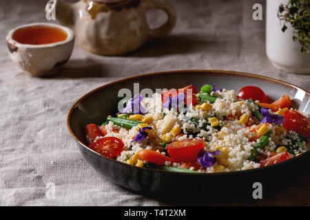 Couscous Salat mit parboiled Gemüse Karotten, grüne Bohnen, Mais, Spinat in Keramik Teller mit Tomaten, Sesam und essbare Blumen, Kaffee Stockfoto