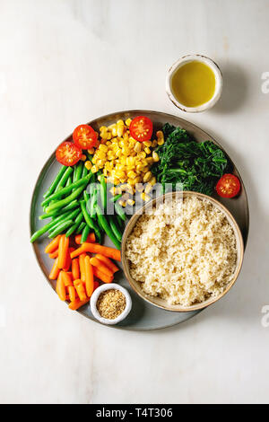Couscous mit parboiled Gemüse Karotten, grüne Bohnen, Mais, Spinat serviert in Keramik Teller mit Tomaten, Sesam, Olivenöl. Vegane Kost Stockfoto