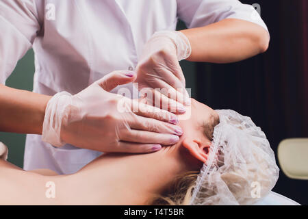 Kosmetiker macht eine bukkale Massage des Gesichts Die Muskeln des Patienten Stockfoto