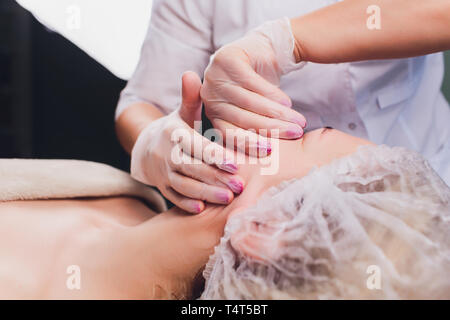 Kosmetiker macht eine bukkale Massage des Gesichts Die Muskeln des Patienten Stockfoto