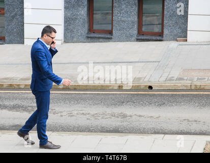 Business Mann in einer blauen classic Anzug sprechen auf mobilen und Rauchen eine Zigarette. Stockfoto