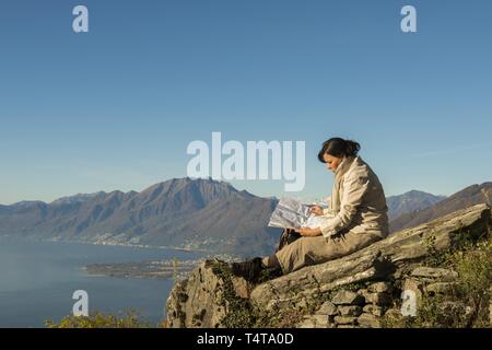 Frau auf einem Berg Entspannen, Lesen einer Karte, See Lago Maggiore im Hintergrund, Tessin, Schweiz Stockfoto