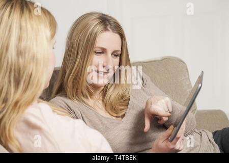 Zwei Frauen sitzen auf einem Sofa mit einem Tablet-PC Stockfoto