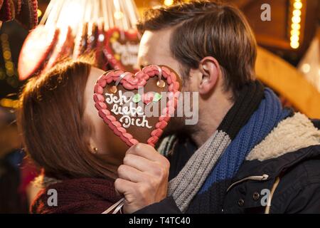 Ein paar Küssen hinter einem Lebkuchenherz, Lebkuchen Herz mit sagt 'Ich liebe dich', der Weihnachtsmarkt, Deutschland, Europa Stockfoto