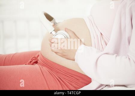 Schwangere Frau mit Kopfhörer auf baby Bauch Stockfoto