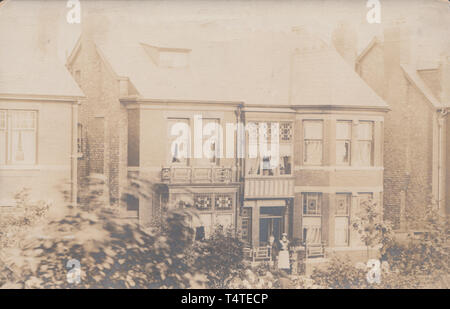 Jahrgang fotografische Postkarte mit einem freistehenden British House. Eine ältere Dame und die Magd posiert vor dem Eigentum. Stockfoto