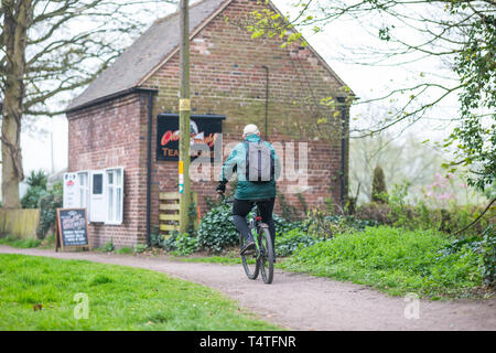 Ansicht der Rückseite des älteren Mann auf dem Fahrrad in grünen Mantel mit Rucksack auf dem Rücken, Radfahren entlang de Canal Leinpfad Vergangenheit offene Teestube isoliert, Frühling Morgen. Stockfoto