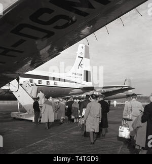 Historische Passagiere der 1960er Jahre, die ein Flugzeug der KLM Royal Dutch Airlines Douglas 7C am Flughafen Anchorage, Alsaka, USA, besteigen. Wie man sehen kann, in dieser Zeit die Formulierung "Koninkluke Luchtvaart Mu. Holland' war auf dem Heck des Flugzeugs. Stockfoto