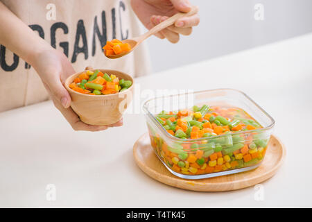 Schöpfkelle aus gedämpftem frisch geernteten jungen Gemüse, einschließlich Crinkle cut geschnittene Karotten, Erbsen und Kartoffeln für eine gesunde Begleitung zum Abendessen Stockfoto