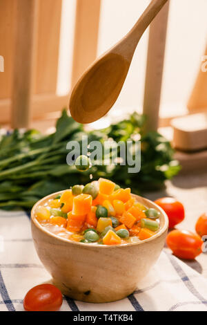 Schöpfkelle aus gedämpftem frisch geernteten jungen Gemüse, einschließlich Crinkle cut geschnittene Karotten, Erbsen und Kartoffeln für eine gesunde Begleitung zum Abendessen Stockfoto