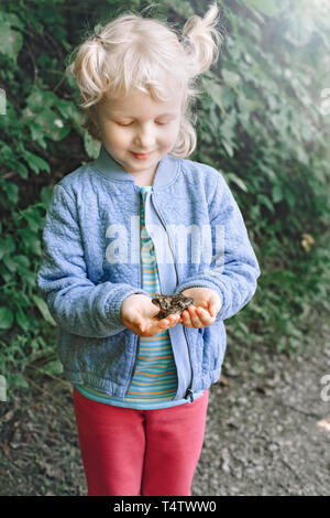 Portrait von cute adorable Kaukasischen blonde Kind Mädchen, dass kleinen Wald Frosch Kröte. Baby Interaktion mit wenig wild Reptile Tier. Pflege von Enviro Stockfoto