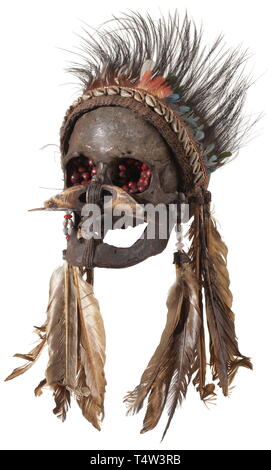 Ein ahnenschädel der Asmat Menschen, Papua Neu Guinea. Dunkel patiniert Schädel eines alten Mannes, der Unterkiefer wird durch eine aufwändige Kabelaufwicklung statt. Die Augenhöhlen mit rötlichen Samen gefüllt, die Nase dekoriert mit einem geschnitzten hohle Knochen. Prächtige Kopfschmuck von textilen Netting, Muscheln und Vogelfedern. Höhe 16 cm. Die Schädel von geschätzten Vorfahren, so genannte "Ndambirkus" waren Objekte der Verehrung. Sie wurden aufwendig dekoriert und an einem sicheren Ort aufbewahrt werden. Die Schädel von Feinden, die so genannte "ndaokus" waren jedoch weniger ehrfürchtig behandelt. T, Additional-Rights - Clearance-Info - Not-Available Stockfoto