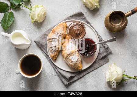 Konzept französisches Frühstück. Tasse Kaffee, weiße Romantische Rosen und frisch gebackene Croissants. Ansicht von oben. Stockfoto