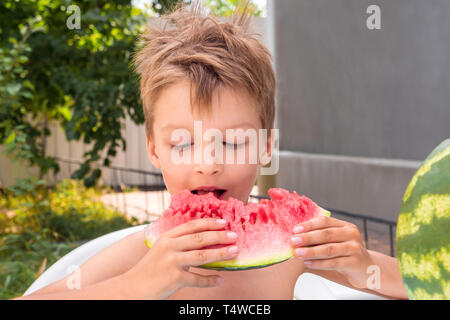 Glückliche Kindheit Konzept. Sommerferien Hintergrund. Schulferien Konzept. Junge, Essen, Wassermelone, draußen im Garten, front, Hinterhof. Reife Stockfoto
