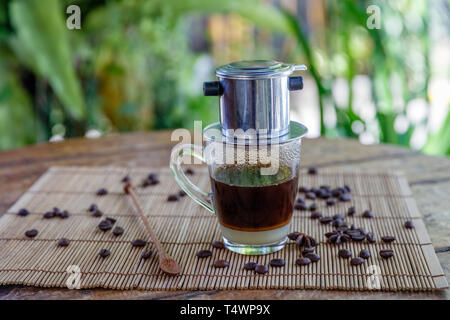 Vietnamesischen traditionellen Drip Filter Kaffee mit süße Kondensmilch in einem Straßencafe. Kaffeebohnen und Cinnamon Stick auf dem Tisch. Stockfoto