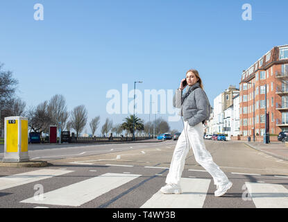 Junges Mädchen gehen über einen Zebrastreifen auf Ihrem Mobiltelefon Stockfoto