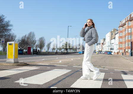 Junges Mädchen gehen über einen Zebrastreifen auf Ihrem Mobiltelefon Stockfoto