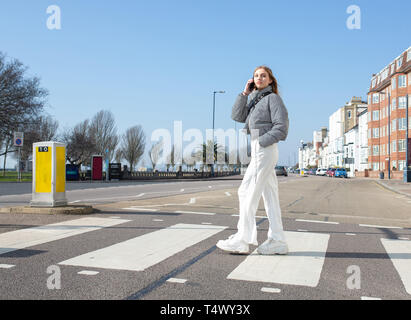 Junges Mädchen gehen über einen Zebrastreifen auf Ihrem Mobiltelefon Stockfoto