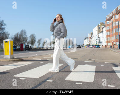 Junges Mädchen gehen über einen Zebrastreifen auf Ihrem Mobiltelefon Stockfoto