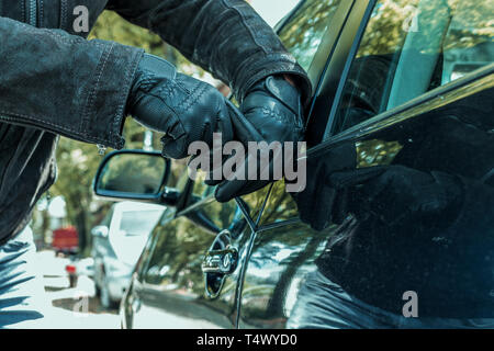 Eine Person mit einer Hand Handschuhe versucht, die Sperre von einem Auto mit einem Schraubendreher in seine Hände auf einer Straße zu brechen Stockfoto